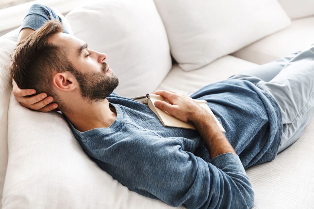 Man in blue shirt napping on couch with book