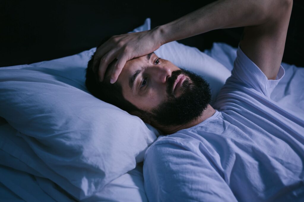 Man in bed holding hand to head unable to sleep