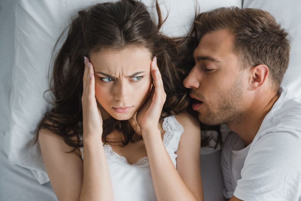 A man snoring in bed next to his wife
